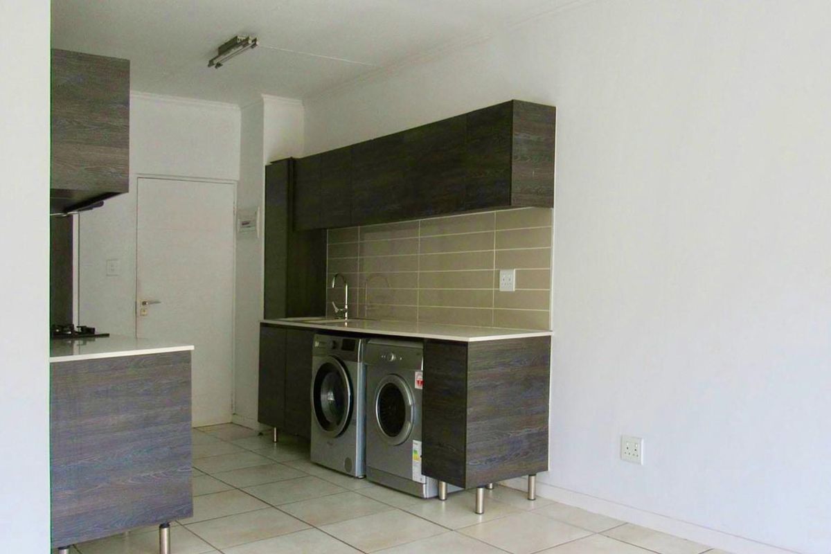 Modern kitchen featuring dark wood-grain cabinetry, light stone countertops, tiled backsplash, and integrated space for laundry appliances.