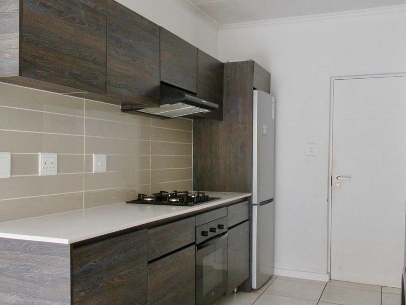Modern kitchen featuring dark wood-grain cabinetry, stone-look countertops, a built-in gas hob, oven, and extractor fan with tiled splashbacks.