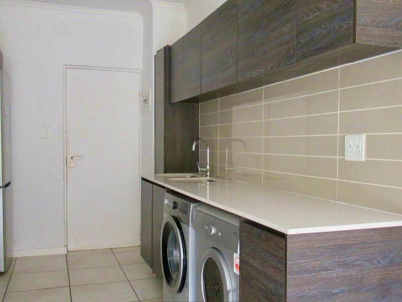 Modern kitchen featuring dark wood cabinetry, stone countertops, tiled backsplash, integrated sink, and built-in oven with extractor fan.