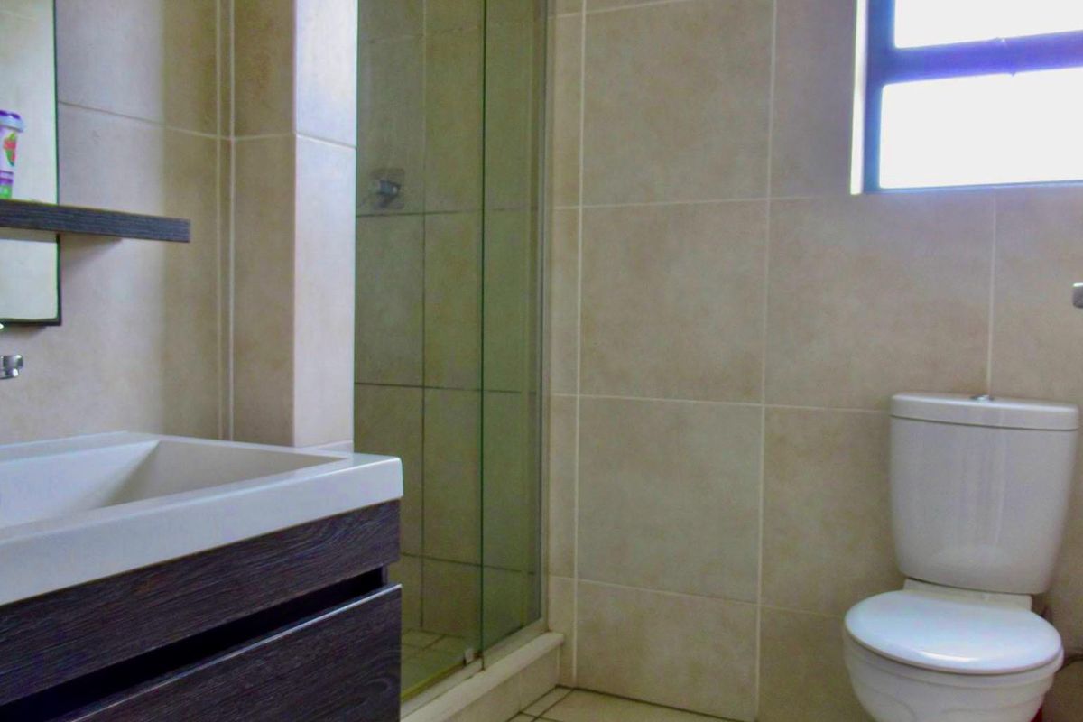 A functional bathroom featuring a modern vanity, a glass-enclosed shower, and neutral wall tiling.