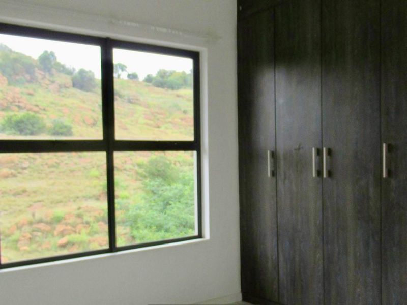 A bright bedroom featuring dark wood built-in cupboards and a large window offering scenic views of the surrounding landscape.