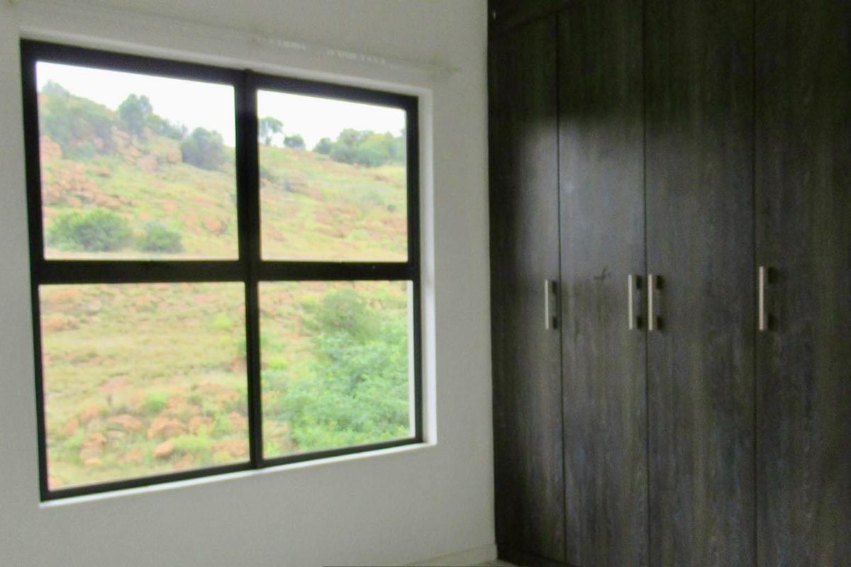 A bright bedroom featuring dark wood built-in cupboards and a large window offering scenic views of the surrounding landscape.