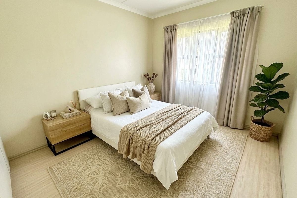 A well-maintained bedroom featuring light-toned laminate flooring, neutral wall finishes, and large windows with fitted curtain tracks.