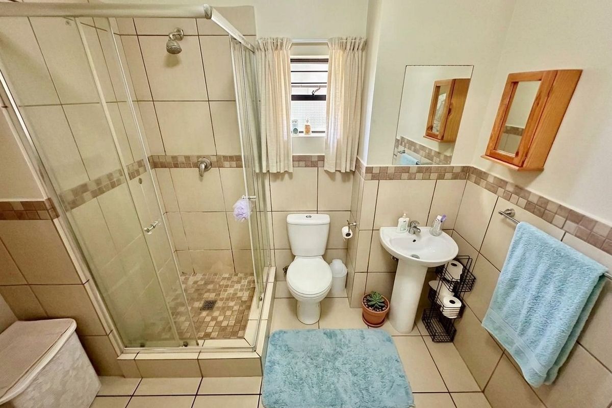 A functional bathroom featuring a glass-enclosed shower, pedestal basin, and toilet, finished with neutral wall and floor tiling.