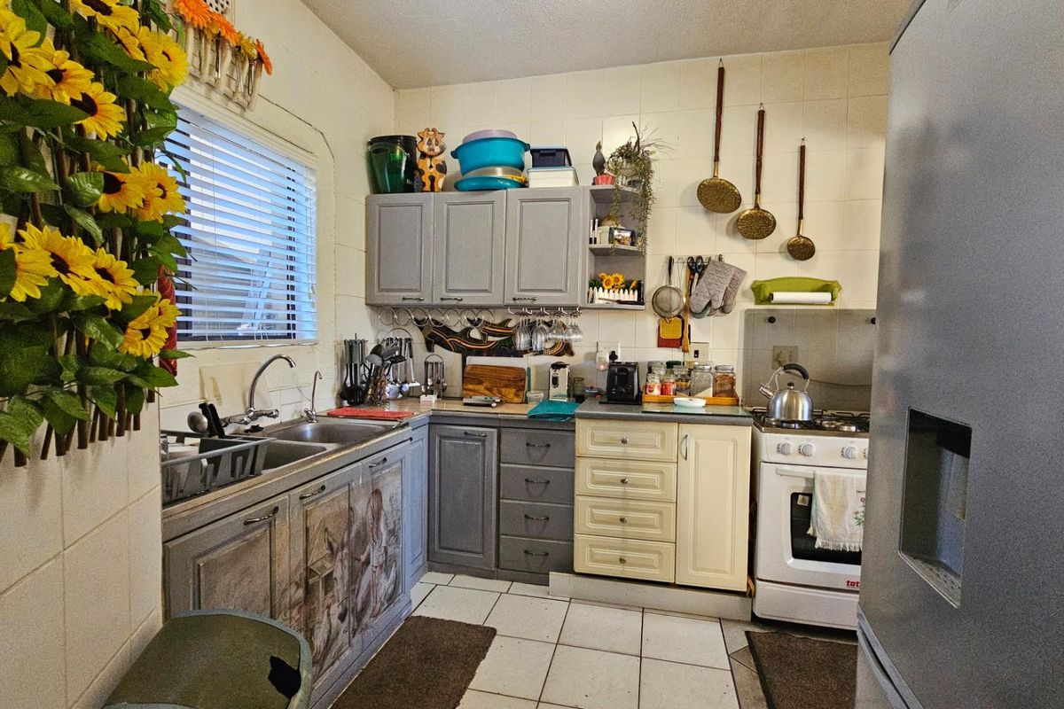 A functional kitchen featuring a double basin sink, tiled splashbacks, and a mix of grey and cream cabinetry with a freestanding stove.