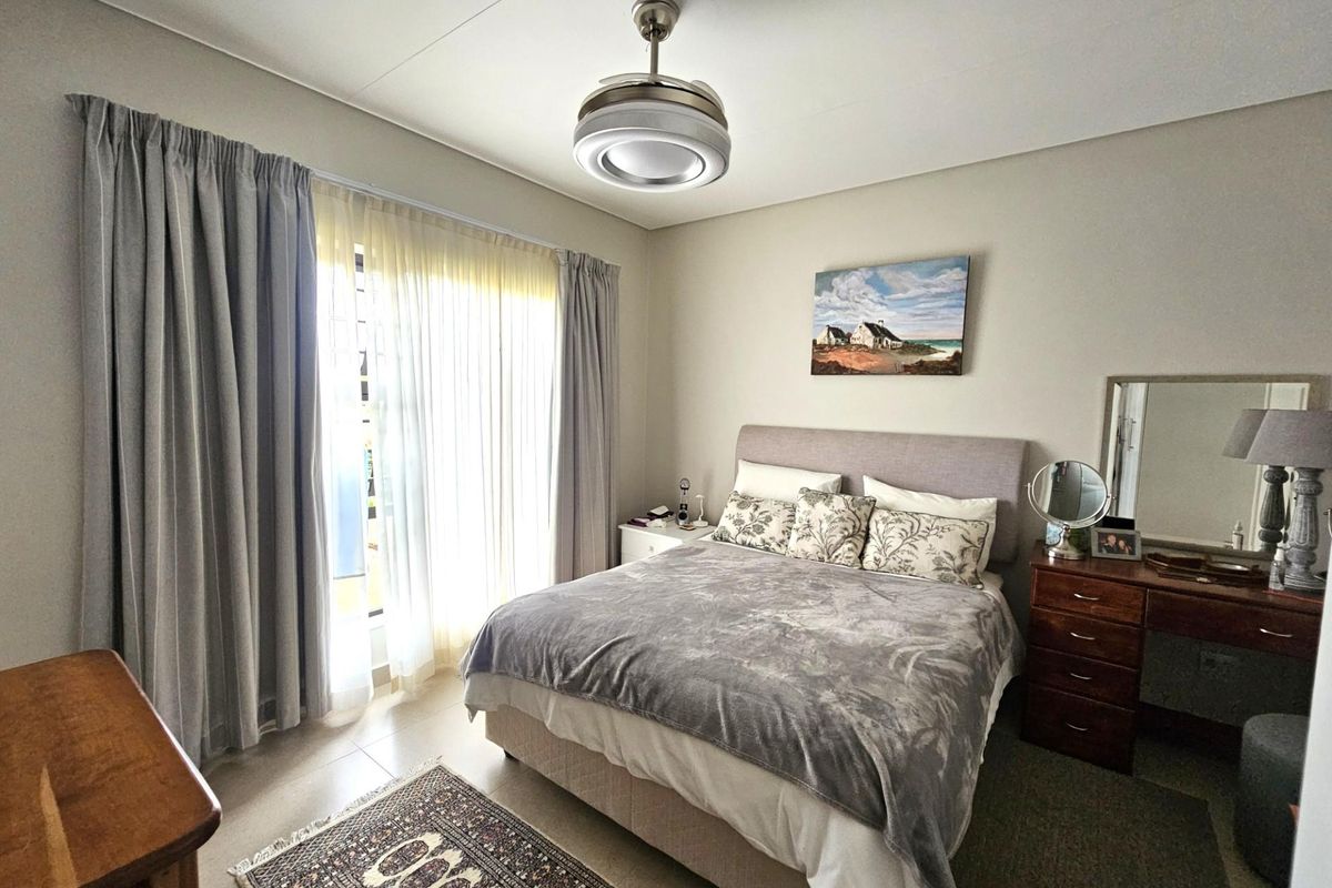 A well-maintained bedroom featuring neutral wall tones, tiled flooring, and a modern ceiling fan with integrated lighting, offering a comfortable and bright living space.