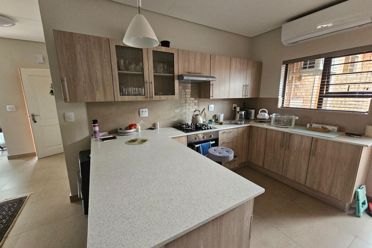 A modern kitchen featuring light wood cabinetry, stone countertops, a built-in gas hob, oven, extractor fan, and a wall-mounted air conditioning unit.