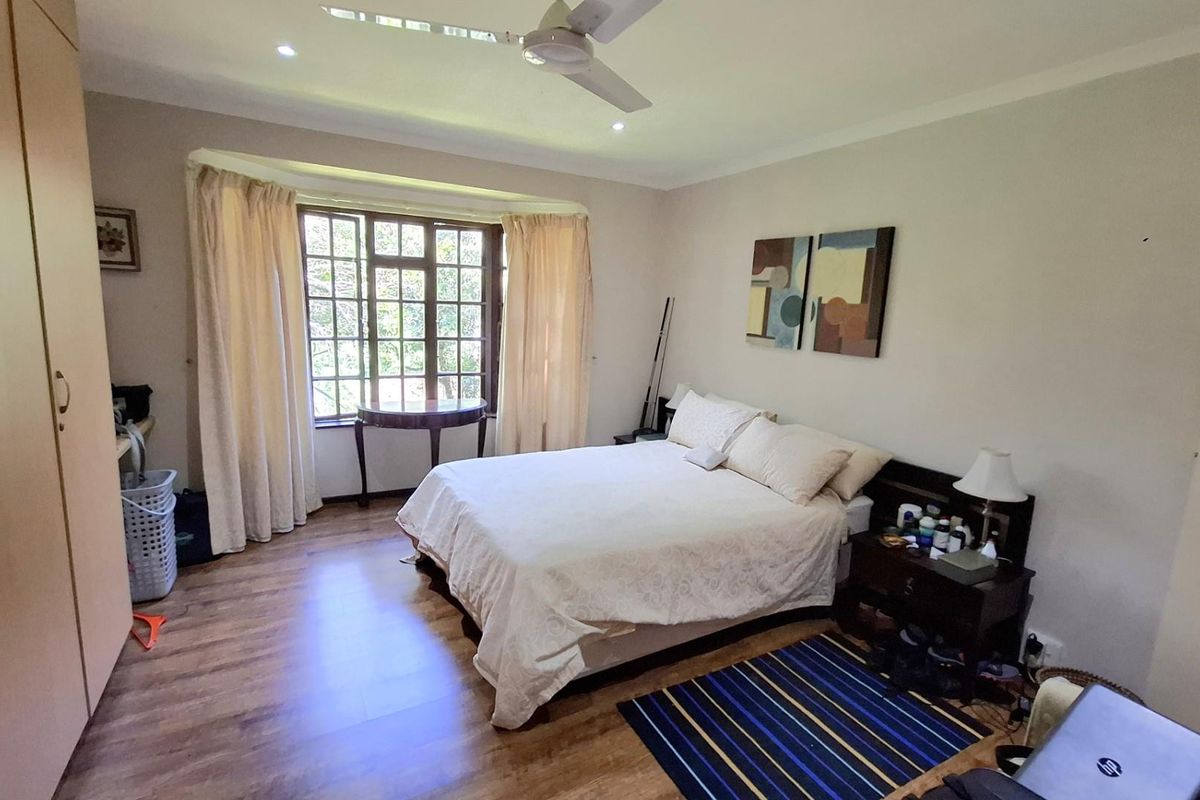 A spacious bedroom featuring wood-look flooring, built-in cabinetry, and a large bay window that provides natural light.