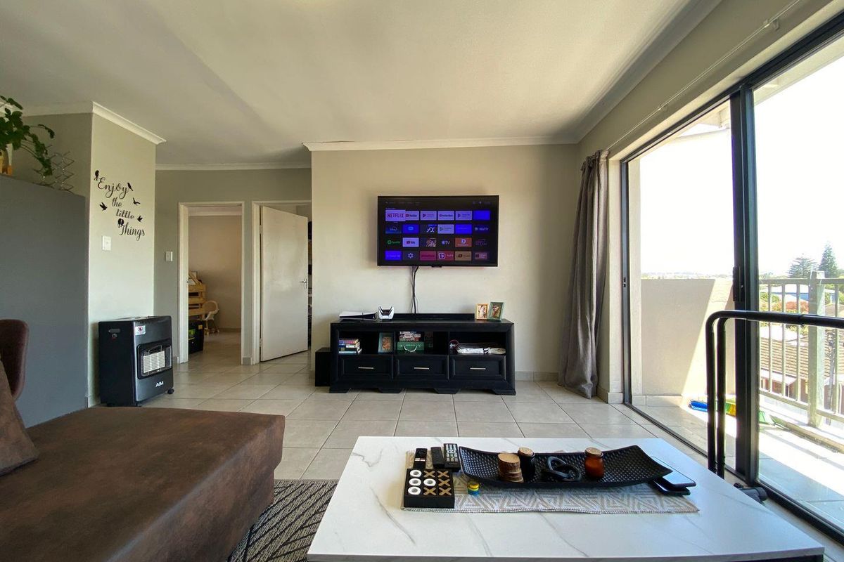 A bright living room featuring tiled flooring and a large sliding glass door providing access to an outdoor balcony area.