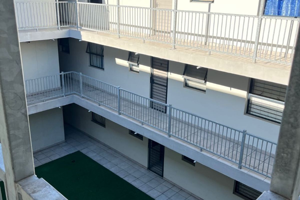 View of the apartment complex courtyard featuring multi-level walkways with metal balustrades and a central artificial grass area.