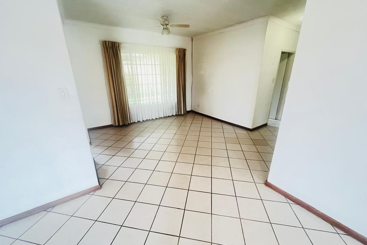 A spacious, open-plan living area featuring neutral ceramic floor tiles, a ceiling fan, and large windows that provide ample natural light.