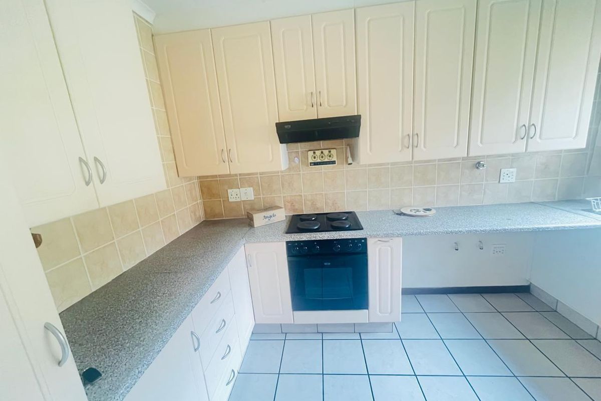 A functional kitchen featuring cream-colored cabinetry, tiled splashbacks, a built-in oven, and a black electric hob with an extractor fan.