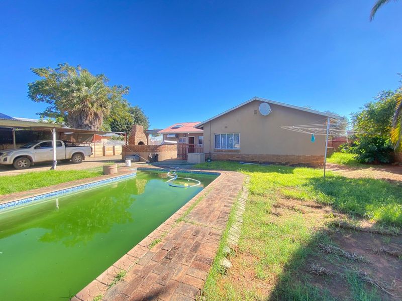 Rear exterior view featuring a swimming pool, brick paved surround, built-in outdoor braai area, and a spacious garden.
