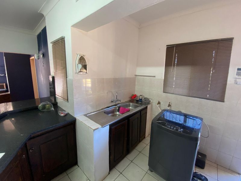 A functional scullery area featuring a stainless steel double sink, dark wood cabinetry, and tiled splashbacks with dedicated plumbing for laundry appliances.