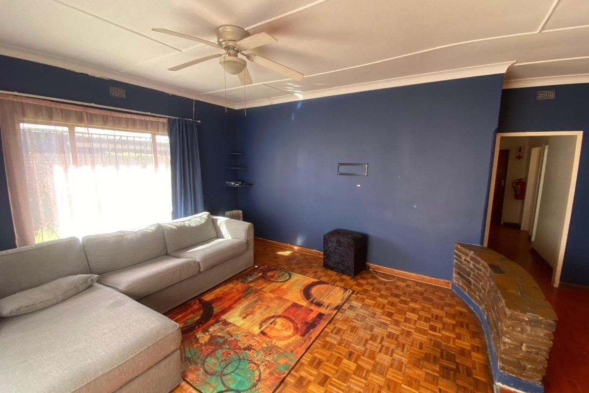 A living room featuring original parquet flooring, a ceiling fan, and a decorative brick feature wall.