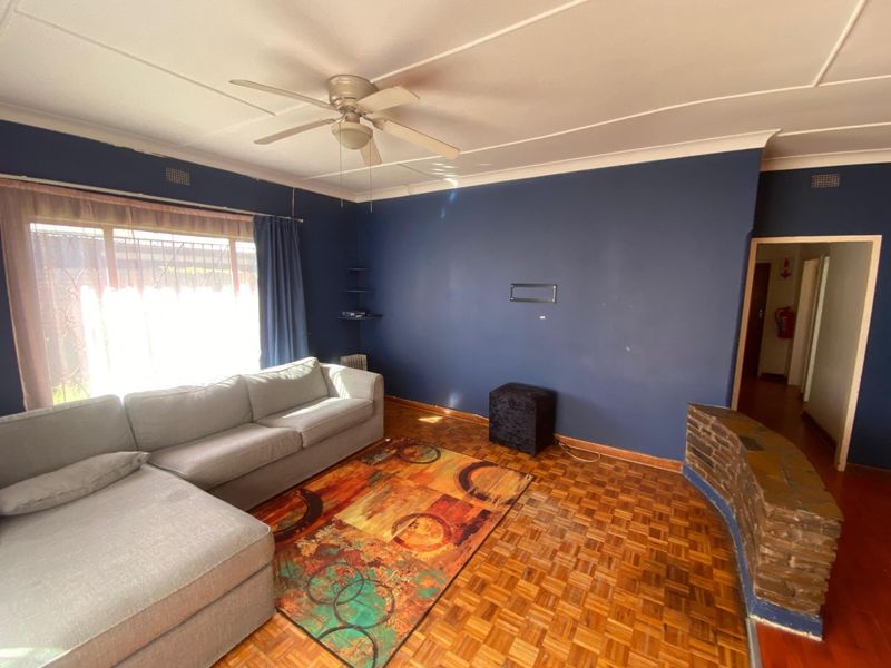 A living room featuring original parquet flooring, a ceiling fan, and a decorative brick feature wall.