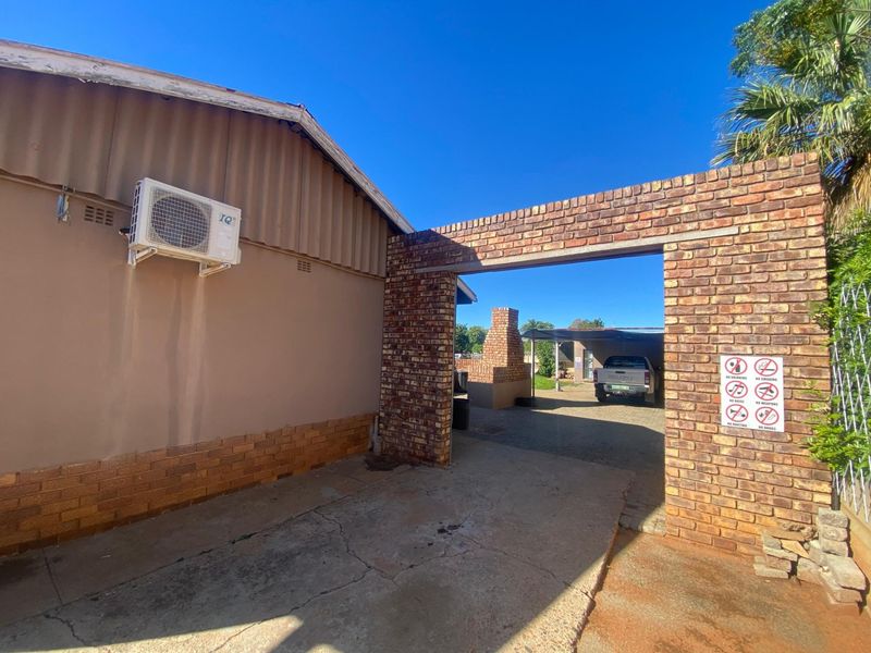 Exterior view of the property featuring a brick archway, concrete driveway, and an external air conditioning unit mounted on the side wall.