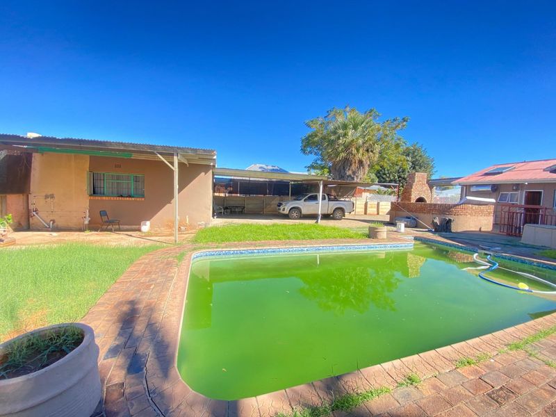 Rear exterior view featuring a swimming pool, covered patio area, and brick-built outdoor fireplace in a spacious backyard setting.