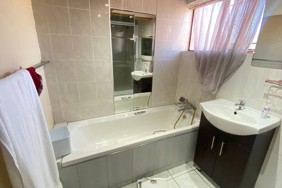A functional bathroom featuring a built-in bathtub with shower mixer, a vanity cabinet with basin, and tiled wall finishes.