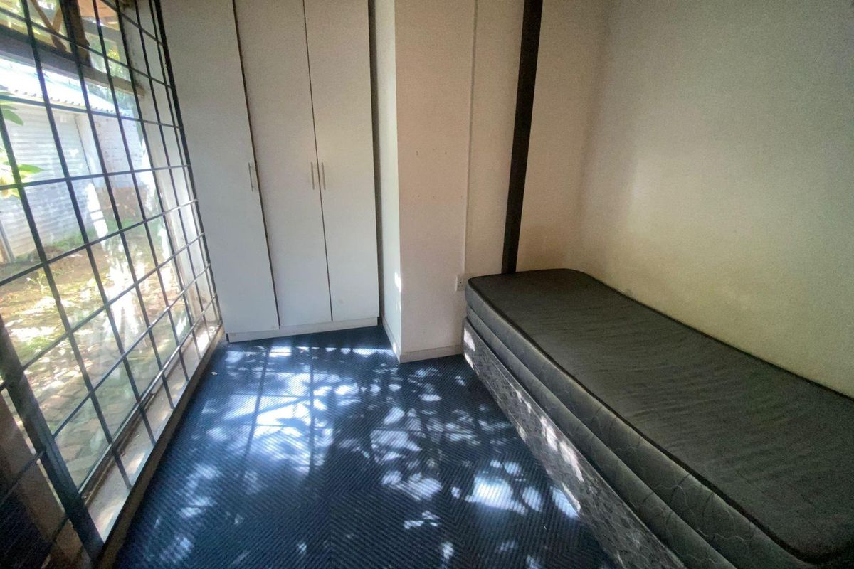 A bedroom featuring built-in cabinetry and large windows with security bars, providing natural light and garden views.