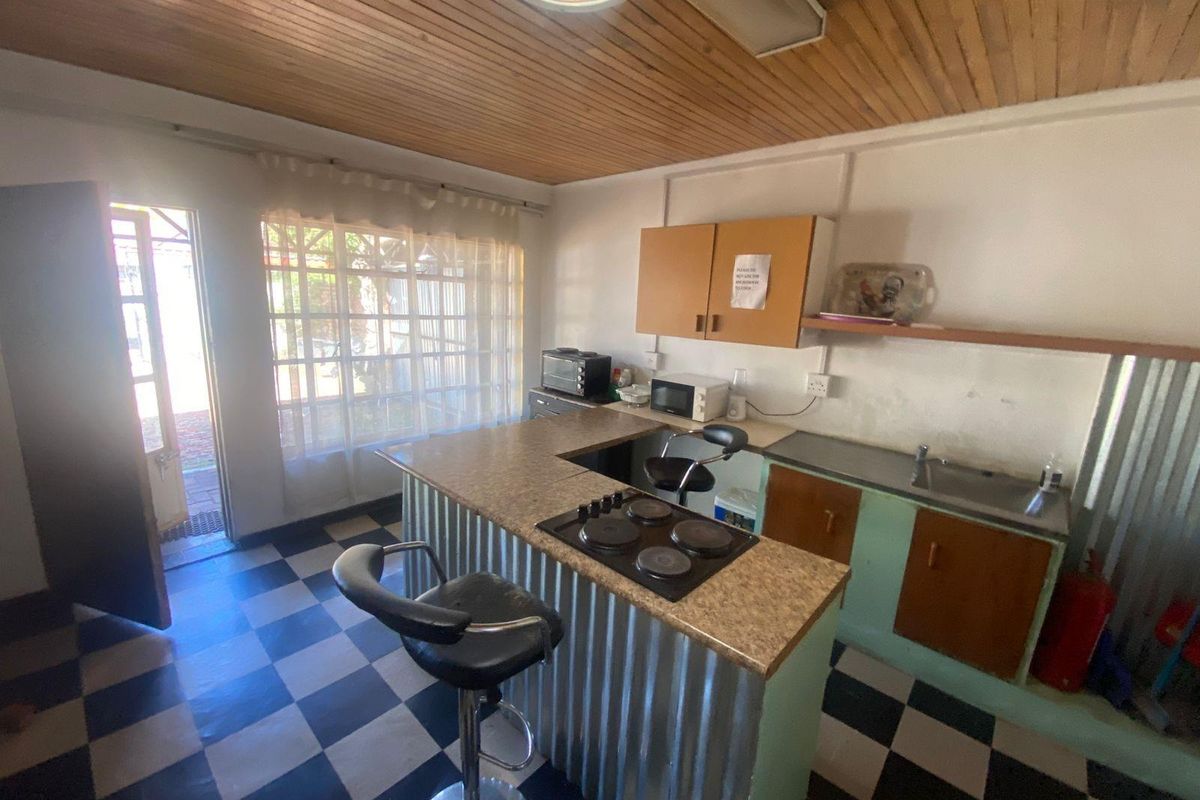 A dated kitchen featuring a corrugated metal breakfast bar, built-in hob, stainless steel sink, and timber-clad ceiling with checkered flooring.