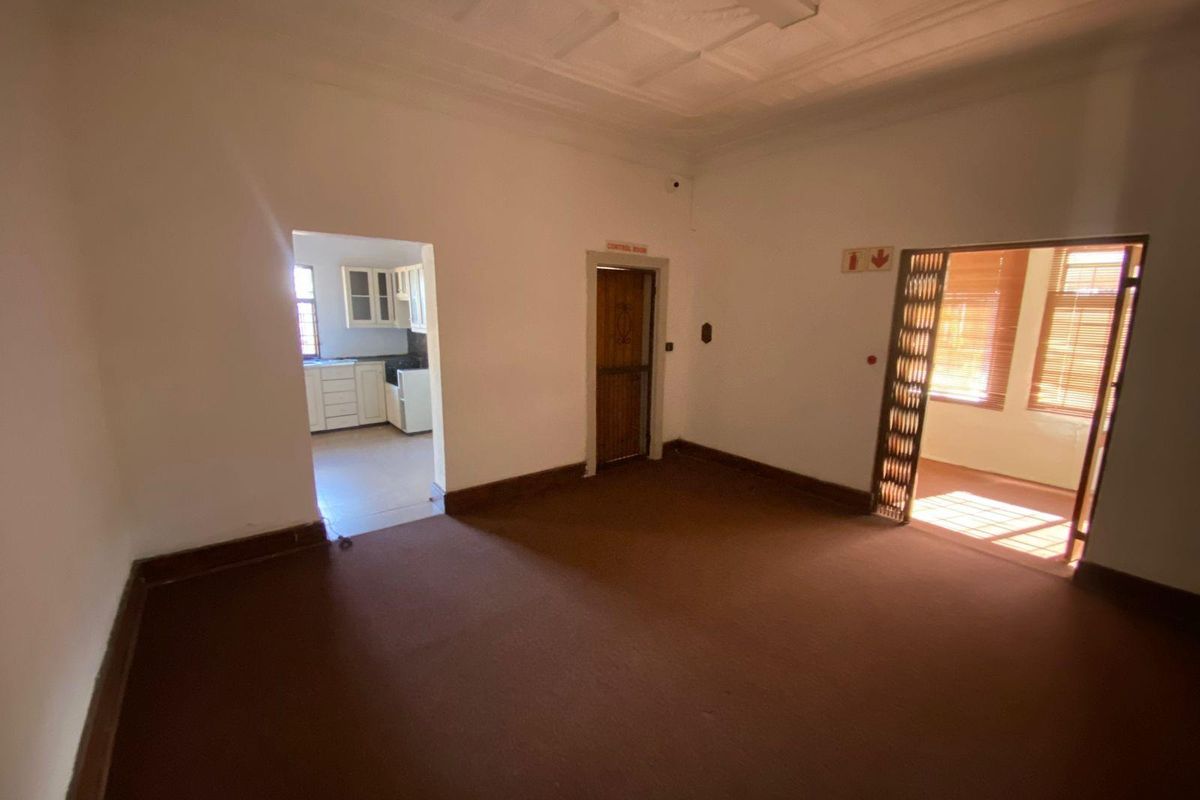 An empty living area featuring high ceilings with decorative molding, carpeted flooring, and direct access to an adjacent kitchen and sunroom.