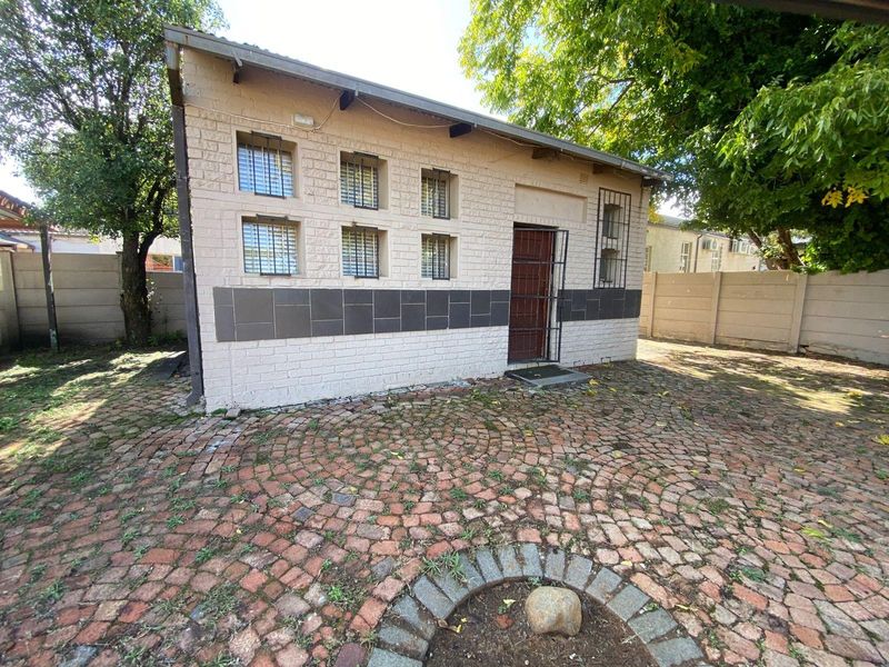 Exterior view of a detached outbuilding featuring brick construction, security bars on windows, and a paved courtyard area.
