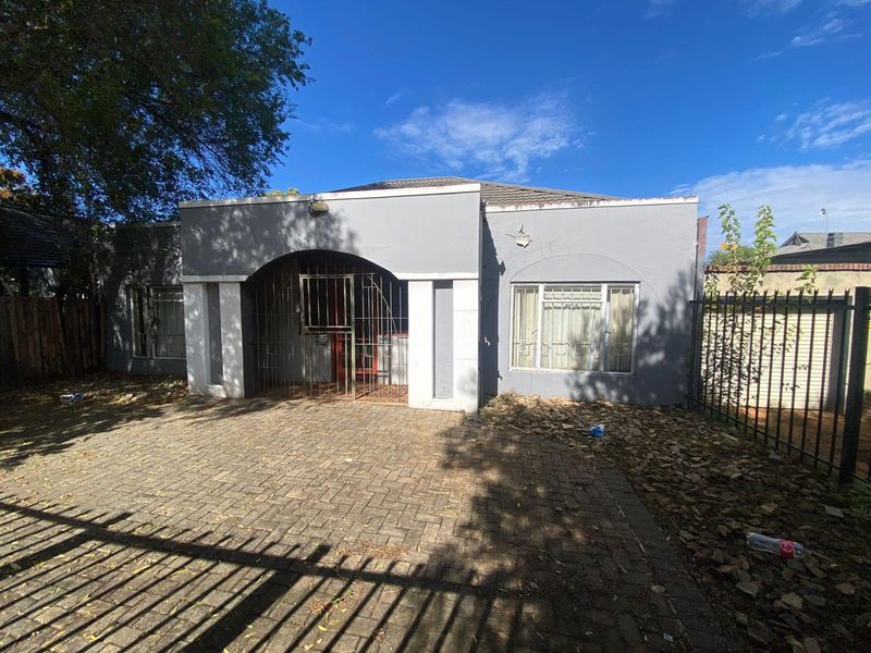 Front exterior view of a single-story house featuring a paved driveway, arched entrance with security gate, and perimeter metal fencing.