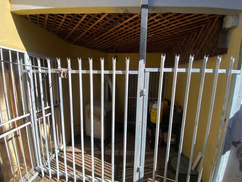 A covered outdoor utility or laundry area featuring a security gate, lattice ceiling, and yellow exterior walls.