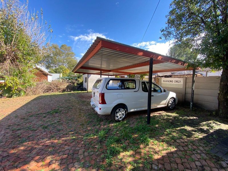 Outdoor carport area with metal roofing structure, situated on a paved driveway with surrounding garden space.