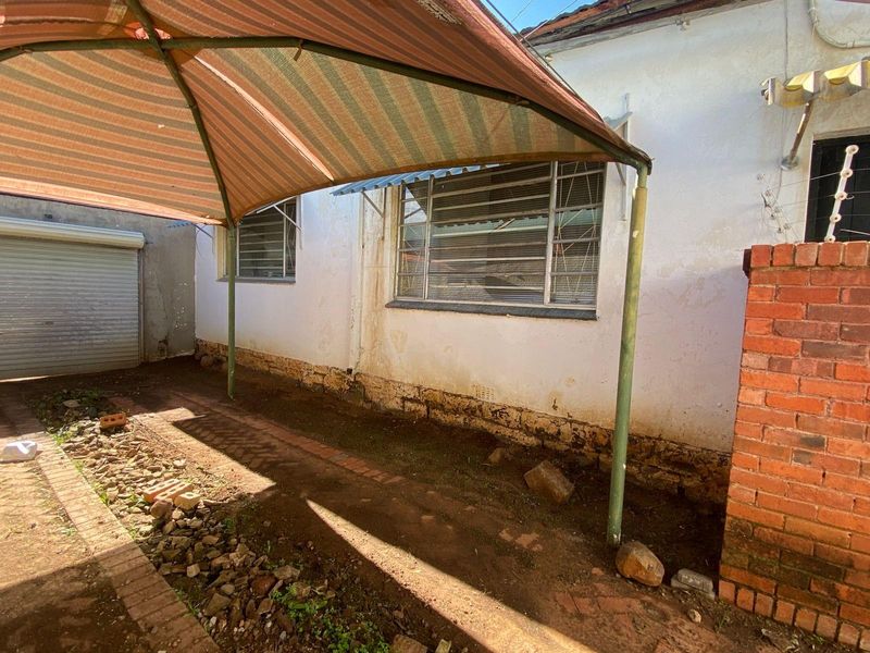 Rear exterior view of the property featuring a basic patio area, weathered brick and plaster walls, and metal-framed windows.