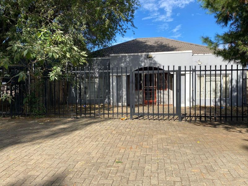 Front view of a single-story house featuring a paved driveway, secure metal perimeter fencing, and a tiled roof.