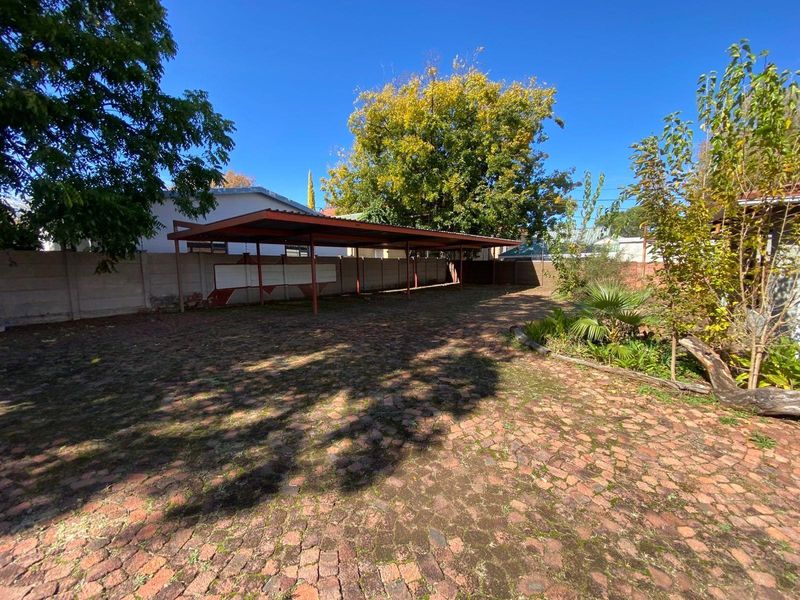 Spacious outdoor area featuring a large covered carport, paved driveway, and established garden borders.