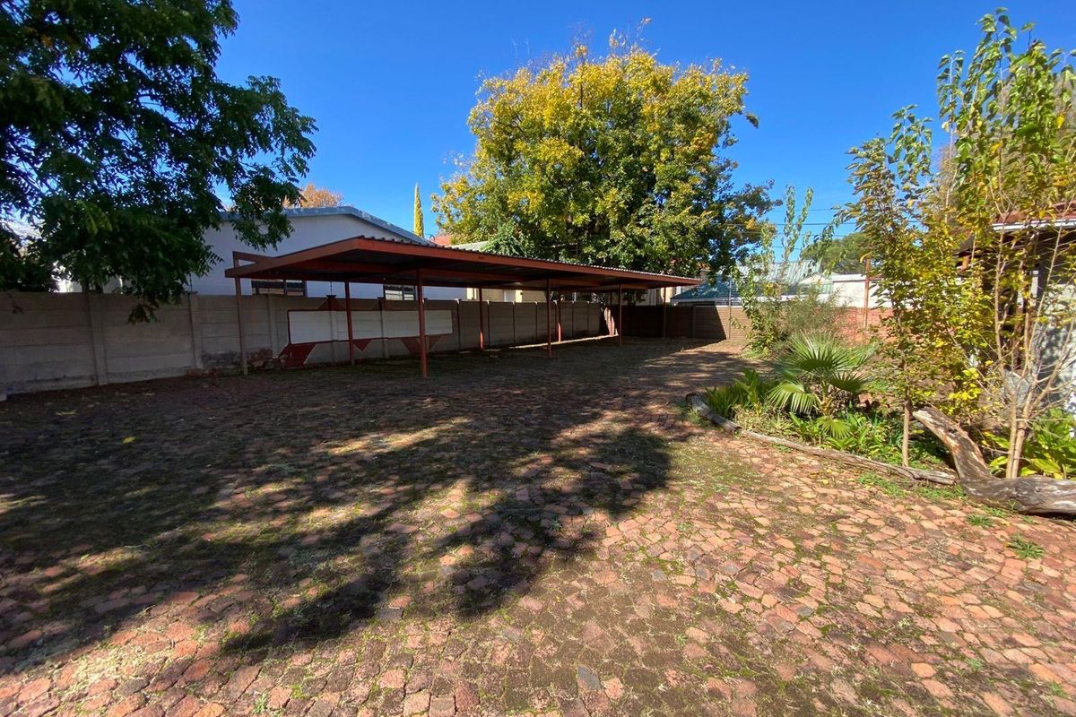 Spacious outdoor area featuring a large covered carport, paved driveway, and established garden borders.