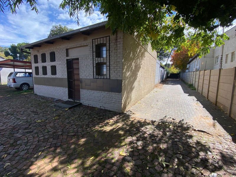 Exterior view of a brick outbuilding or garage structure featuring security bars on windows and a paved driveway area.