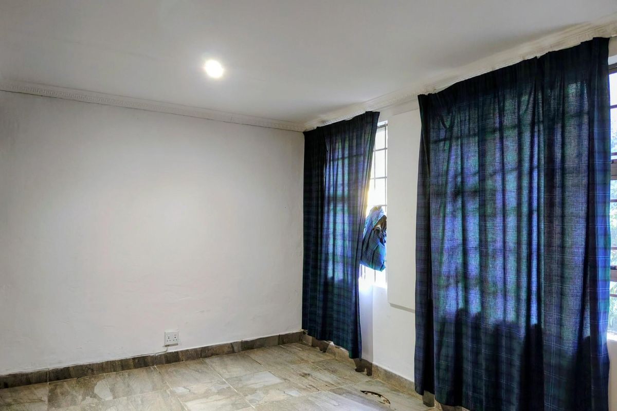 An empty bedroom featuring tiled flooring, ceiling cornice, and natural light through large windows. The space requires minor repairs to flooring and wall finishes.
