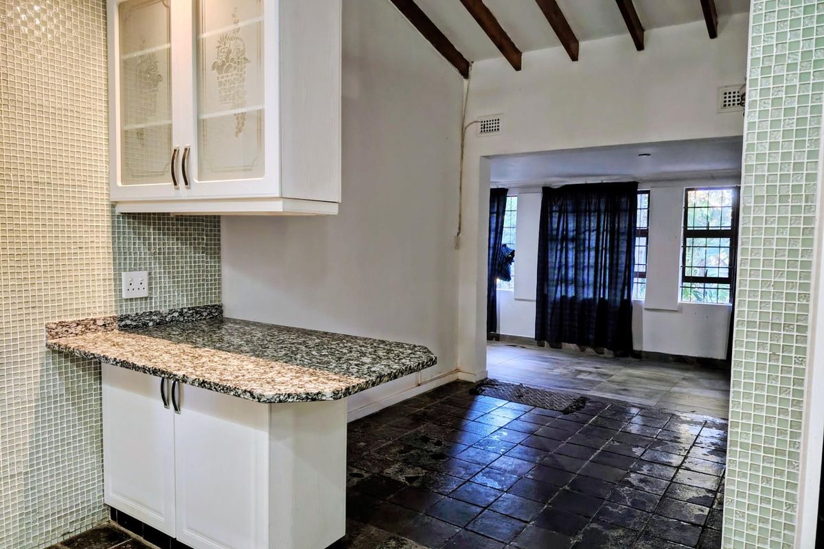 Kitchen area featuring granite countertops, mosaic tile backsplash, and exposed timber ceiling beams, leading into an adjacent living space with tiled flooring.