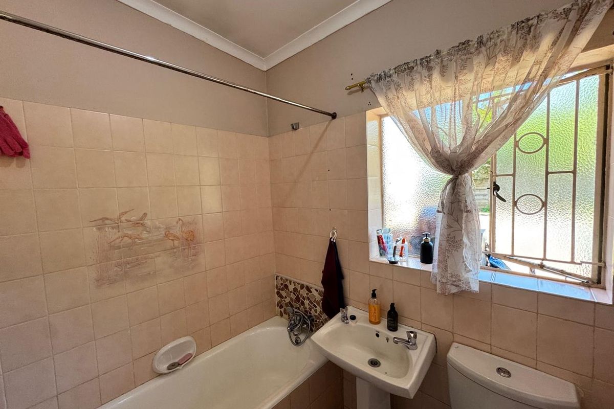 A dated bathroom featuring a standard bathtub, pedestal basin, and toilet with original wall tiling and security bars on the window.