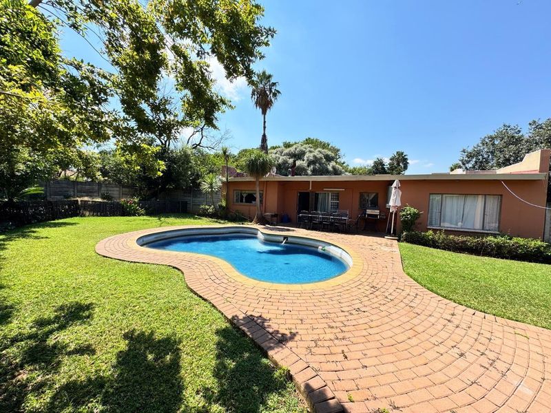 Spacious rear garden featuring a kidney-shaped swimming pool with brick paving, established lawn, and direct access to the main house.