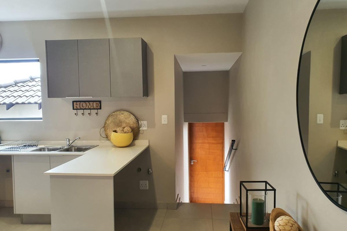 Modern kitchen area featuring sleek grey cabinetry, stone countertops, and a stainless steel sink, with an adjacent staircase leading to another level.