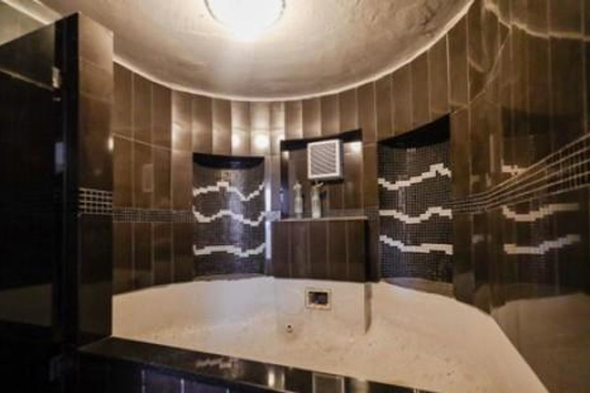 A bathroom featuring a built-in corner bathtub with dark tiled surround and decorative mosaic accents.
