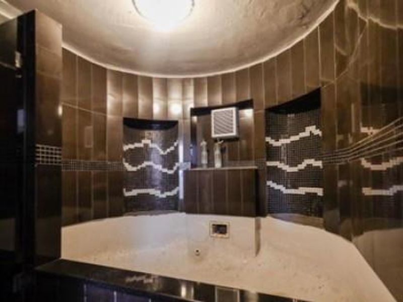 A bathroom featuring a built-in corner bathtub with dark tiled surround and decorative mosaic accents.