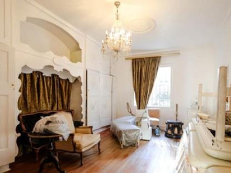 A spacious room featuring ornate built-in cabinetry, decorative ceiling molding, a crystal chandelier, and polished timber flooring.