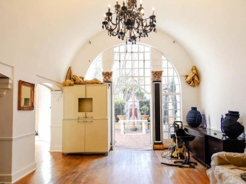 Spacious living area featuring a barrel-vaulted ceiling, ornate chandelier, and large arched window providing natural light and access to the outdoor courtyard.