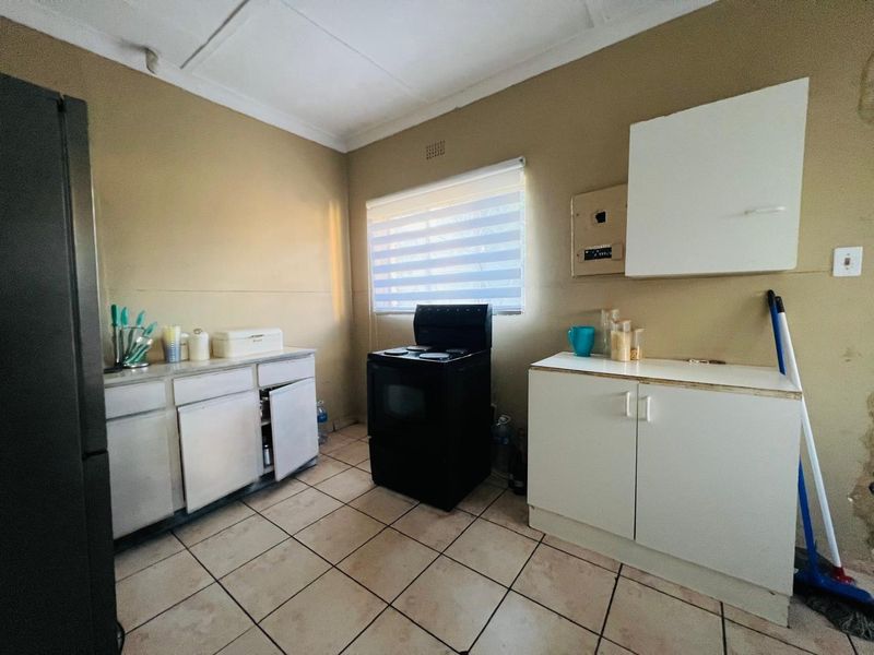 A functional kitchen space featuring basic cabinetry, a freestanding stove, tiled flooring, and a window with a roller blind.