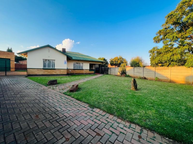 A well-maintained single-story house featuring a paved driveway, manicured front lawn, and secure perimeter fencing.