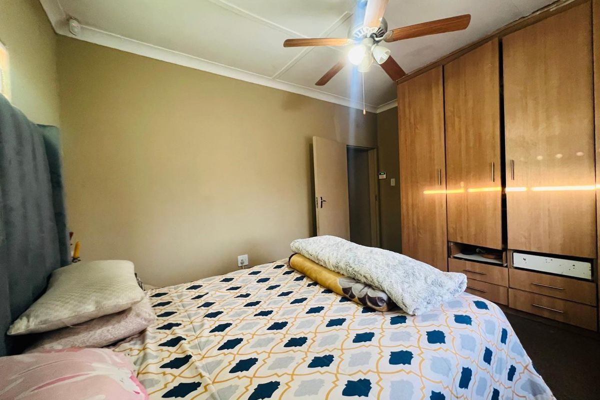 A bedroom featuring built-in wooden wardrobes, a ceiling fan, and neutral wall finishes.