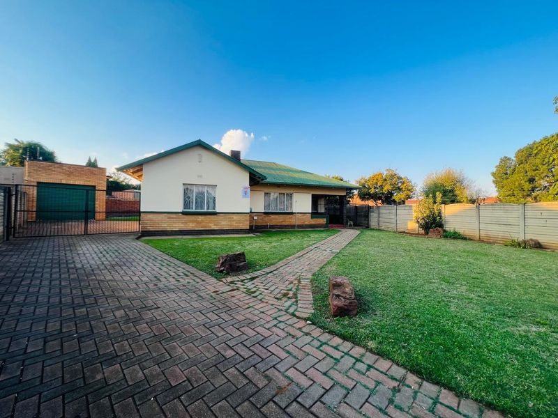 A well-maintained single-story residential home featuring a paved driveway, manicured front lawn, and secure perimeter fencing.