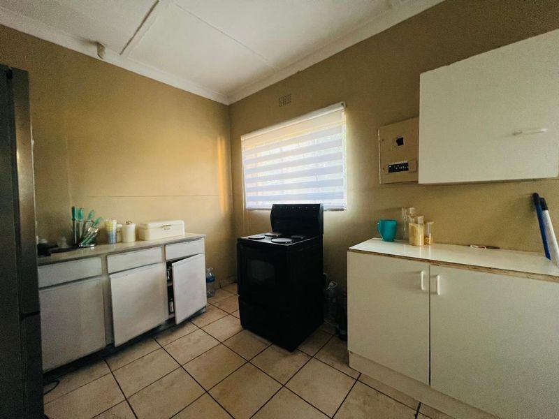 A functional kitchen featuring tiled flooring, basic white cabinetry, and a freestanding stove, offering a practical layout with potential for modernization.