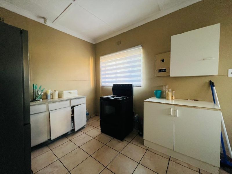 A functional kitchen featuring tiled flooring, white cabinetry, and a freestanding stove, offering a practical layout with potential for modernization.